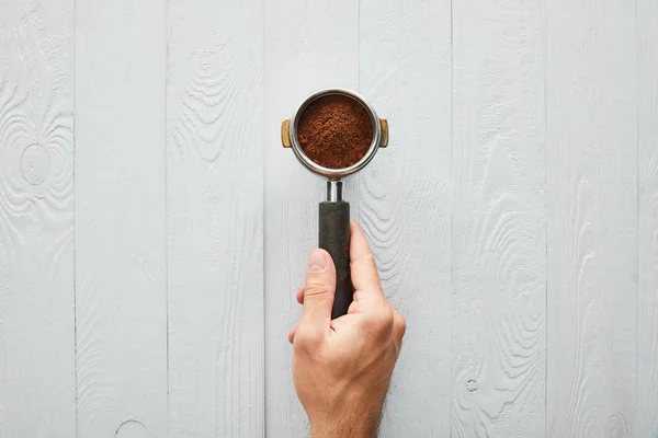 Vue de dessus de l'homme tenant le portafilter avec du café sur la surface en bois blanc — Photo de stock