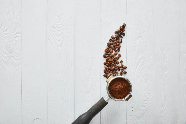 Draufsicht auf Portafilter mit Kaffee auf weißer Holzoberfläche mit Kaffeebohnen — Stockfoto