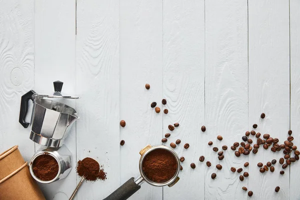 Vue de dessus du portafilter près des parties séparées de la cafetière geyser, des tasses en papier et de la cuillère sur une surface en bois blanc — Photo de stock