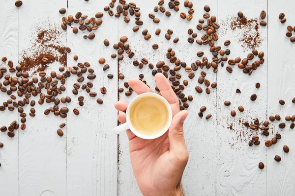 Vista superior do homem segurando xícara de café em seu braço sob a superfície de madeira branca com grãos de café — Fotografia de Stock