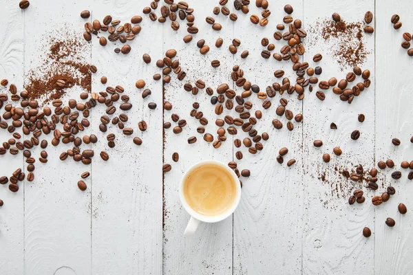Біла чашка з кавою на білій дерев'яній поверхні з кавовими зернами — стокове фото