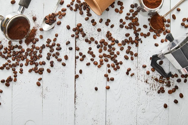 Draufsicht auf Geysir-Kaffeemaschine, Portafilter, Löffel und Pappbecher auf weißer Holzoberfläche mit Kaffeebohnen — Stockfoto