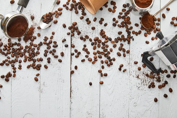 Vista superior de la cafetera géiser, portafilter, cucharas y taza de papel en la superficie de madera blanca con granos de café - foto de stock