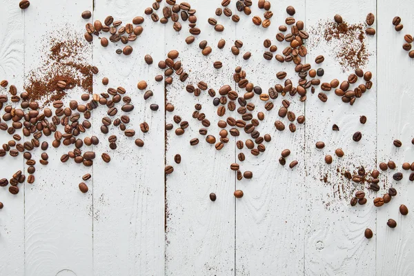 Superfície de madeira branca com grãos de café espalhados e café moído — Fotografia de Stock