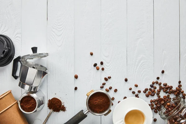 Top view of portafilter, spoon, paper cups, geyser coffee maker and glass jar with coffee on white wooden surface — Stock Photo