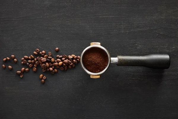 Top view of portafilter with coffee on dark wooden surface with scattered coffee beans — Stock Photo