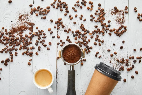 Vista superior da xícara de papel entre portafilter e xícara de café expresso na superfície de madeira branca com grãos de café — Fotografia de Stock