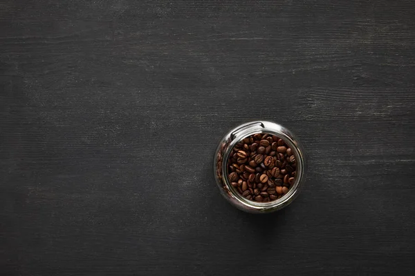 Glass jar with coffee beans on dark wooden surface — Stock Photo