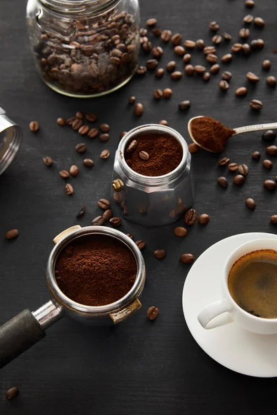 Macchina da caffè Geyser vicino a tazza di caffè, portafiltro, cucchiaio e vaso di vetro su una superficie di legno scuro con chicchi di caffè — Foto stock