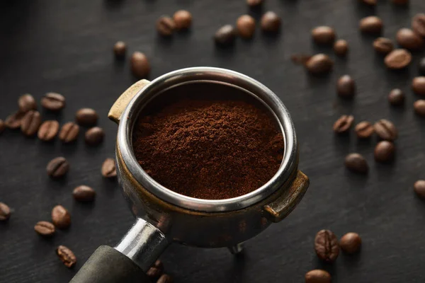 Portafilter filled with fresh coffee on dark wooden surface with coffee beans — Stock Photo
