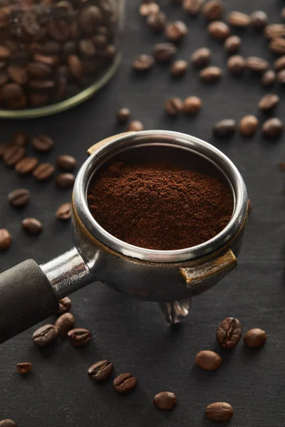 Portafilter filled with ground coffee near glass jar on dark wooden surface — Stock Photo