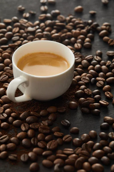 Copo branco com café expresso na superfície escura com grãos de café — Fotografia de Stock