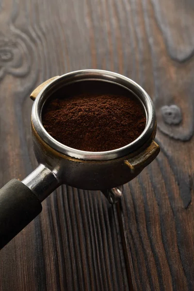 Portafilter filled with ground coffee on dark wooden surface — Stock Photo