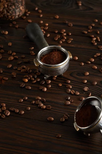 Portafilters with ground coffee on dark wooden surface with coffee beans — Stock Photo