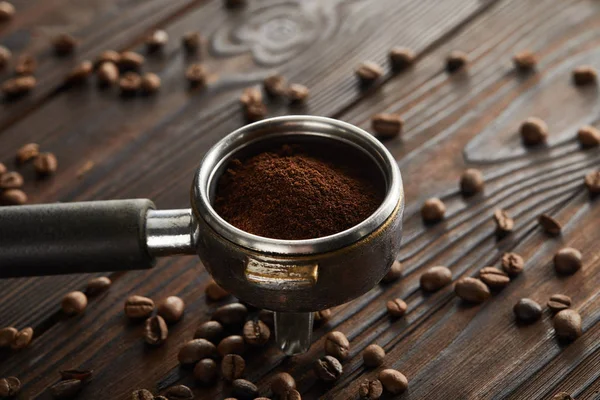 Portafilter filled with fresh ground coffee on dark wooden surface with coffee beans — Stock Photo