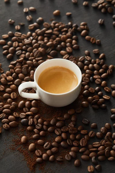 Copo branco com café na superfície escura com grãos de café espalhados — Fotografia de Stock