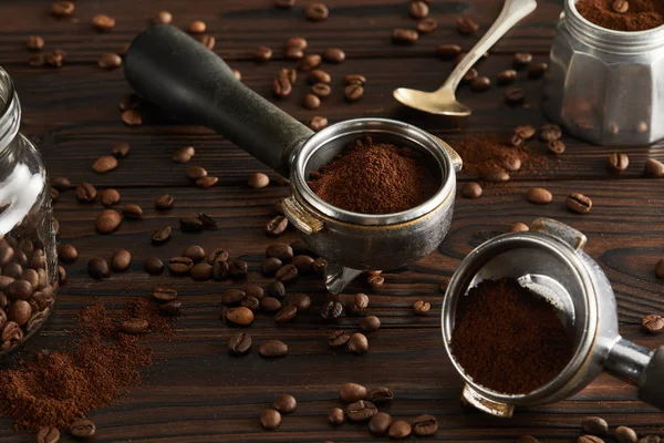 Portafilters near spoon, glass jar and parts of geyser coffee maker on dark wooden surface — Stock Photo