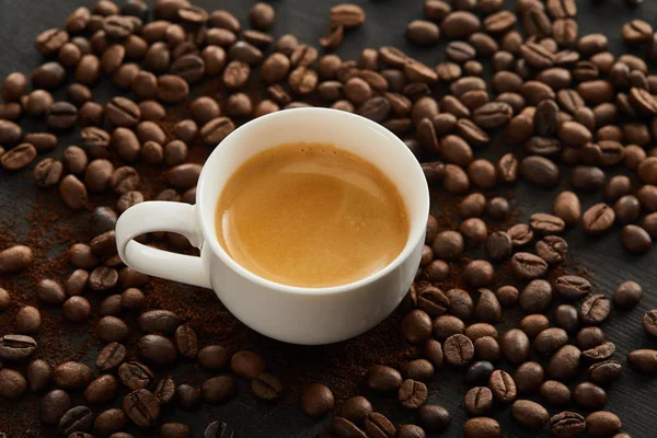 Copo de cerâmica branca com café expresso na superfície com grãos de café espalhados — Fotografia de Stock