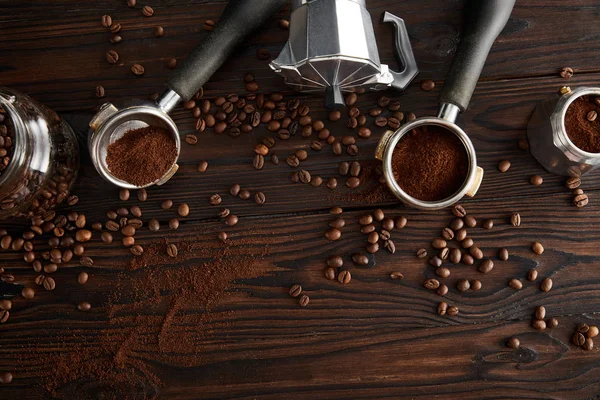 Vista superior de la cafetera géiser entre portafilters y tarro de vidrio en la superficie de madera oscura con granos de café - foto de stock