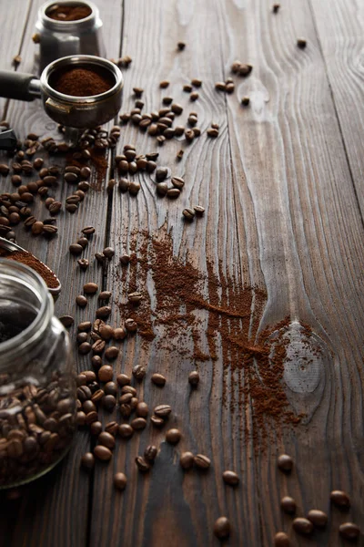Pot en verre près de portafilter et une partie de la cafetière geyser sur la surface en bois sombre avec des grains de café — Photo de stock