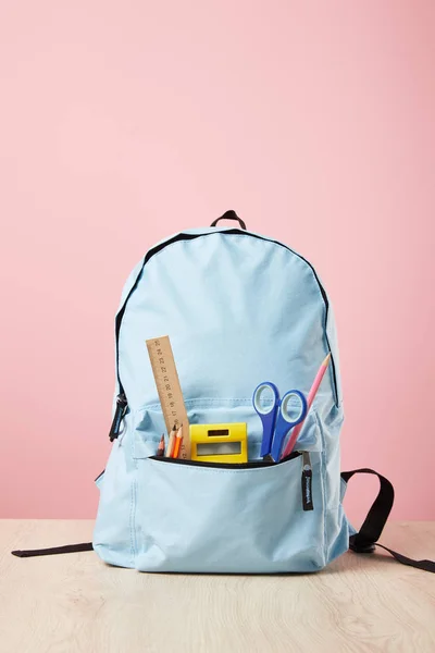 Mochila escolar azul con suministros en bolsillo aislado en rosa - foto de stock