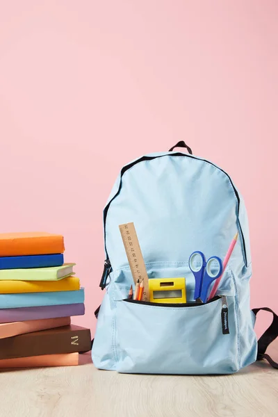 Mochila azul escola com suprimentos no bolso perto de pilha de livros isolados em rosa — Fotografia de Stock