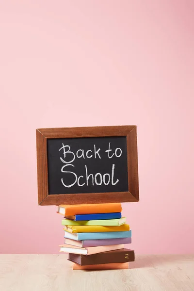 Pila de libros con pizarra con letras de vuelta a la escuela aisladas en rosa - foto de stock