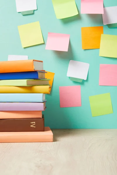 Pilha de livros na mesa perto de notas pegajosas multicoloridas na parede turquesa — Fotografia de Stock