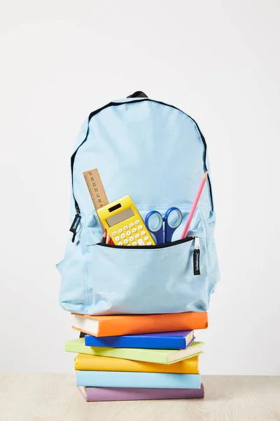 Mochila azul con suministros en bolsillo en libros aislados en blanco - foto de stock