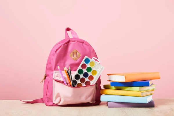 Pink backpack with supplies in pocket near colorful books isolated on pink — Stock Photo