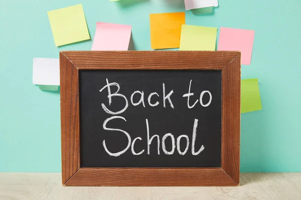 Chalkboard with back to school lettering near multicolored sticky notes on turquoise wall — Stock Photo