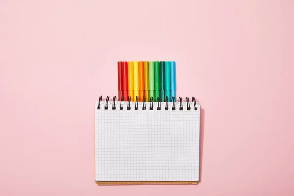 Vista superior de canetas de feltro multicoloridas perto de notebook em branco isolado em rosa — Fotografia de Stock