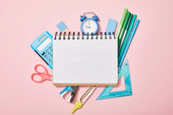 Vista superior de los útiles escolares cerca del cuaderno en blanco aislado en rosa — Stock Photo