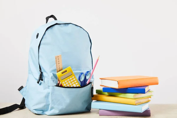 Mochila azul com material escolar perto de livros isolados em branco — Fotografia de Stock