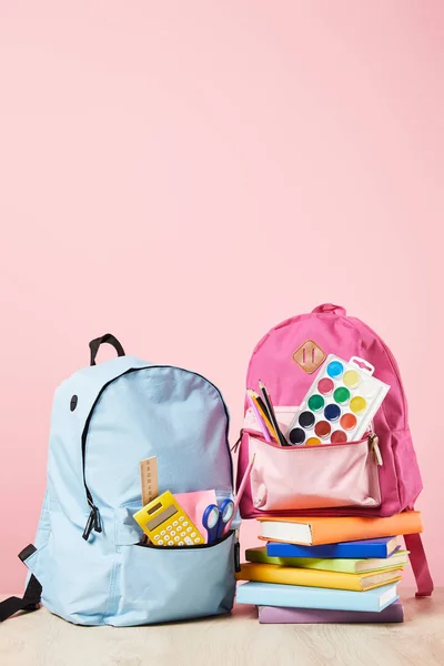 Blue and pink backpacks with school supplies near stack of books isolated on pink — Stock Photo