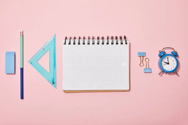 Piso con útiles escolares cerca de cuaderno en blanco aislado en rosa - foto de stock