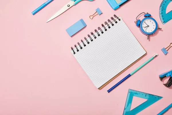 Tendido plano con útiles escolares azules y cuaderno en blanco aislado en rosa - foto de stock