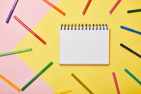 Draufsicht auf leeres Notizbuch mit bunten Filzstiften auf rosa und gelben Hintergrund — Stockfoto
