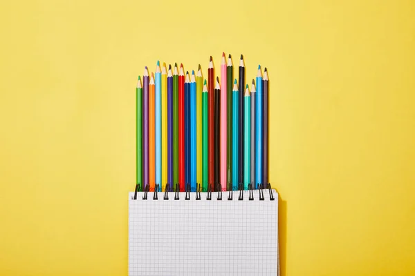 Вид зверху кольорових олівців біля порожнього записника на жовтому — стокове фото