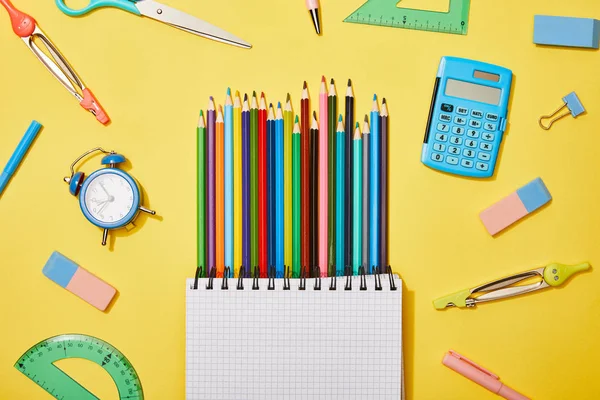 Vista superior de lápis coloridos caderno em branco entre os materiais escolares em amarelo — Fotografia de Stock