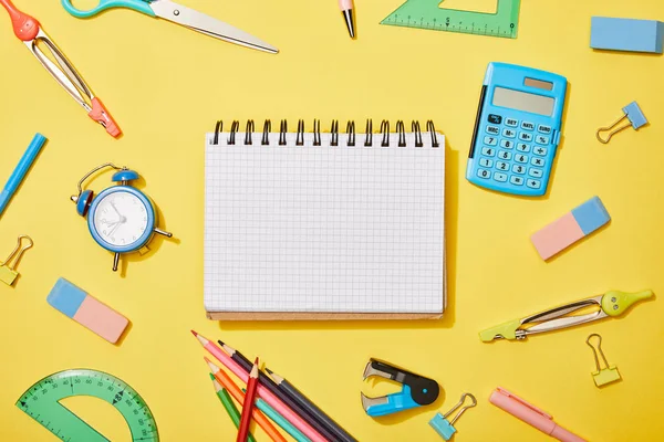 Top view of blank notebook among school supplies on yellow background — Stock Photo