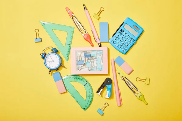 Top view of school supplies scattered near box with clips on yellow background — Stock Photo