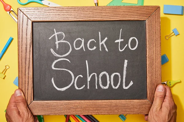 Vista recortada del hombre sosteniendo pizarra con letras de vuelta a la escuela - foto de stock