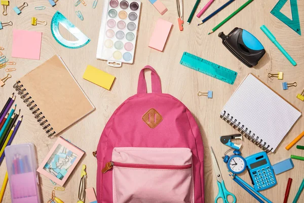 Top view of various school supplies with pink backpack on wooden desk — Stock Photo