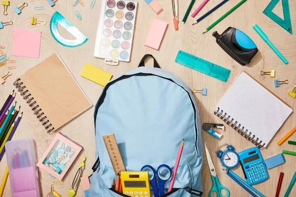 Vista superior de vários materiais escolares com mochila azul na mesa de madeira — Fotografia de Stock