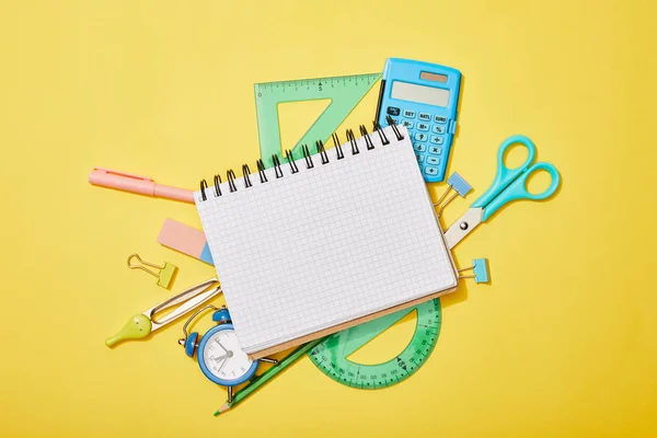 Top view of school supplies scattered on yellow background with blank notebook — Stock Photo