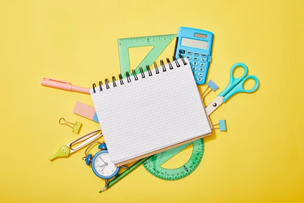 Vue du dessus des fournitures scolaires éparpillées sur fond jaune avec carnet vierge — Photo de stock