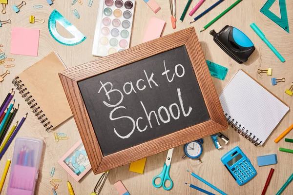 Top view of various school supplies and chalkboard with back to school lettering on wooden desk — Stock Photo