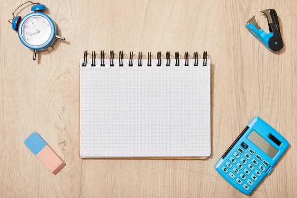 Vue du dessus du bloc-notes vide près du caoutchouc, horloge et calculatrice sur bureau en bois — Photo de stock