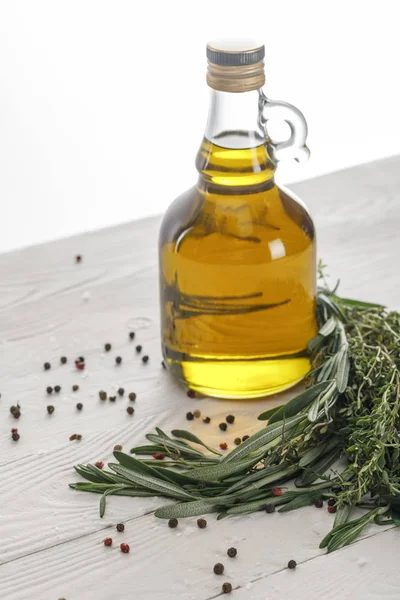 Bottle of oil near rosemary and thyme bungs, scattered red and black peppercorns on white wooden surface isolated on white — Stock Photo